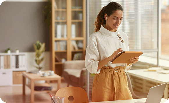 A professional standing at her desk, reviewing progress on a tablet