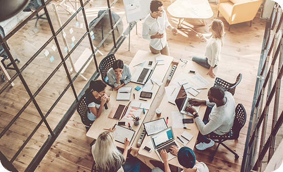 An overhead view of a team working together around a shared table of laptops and planning notes